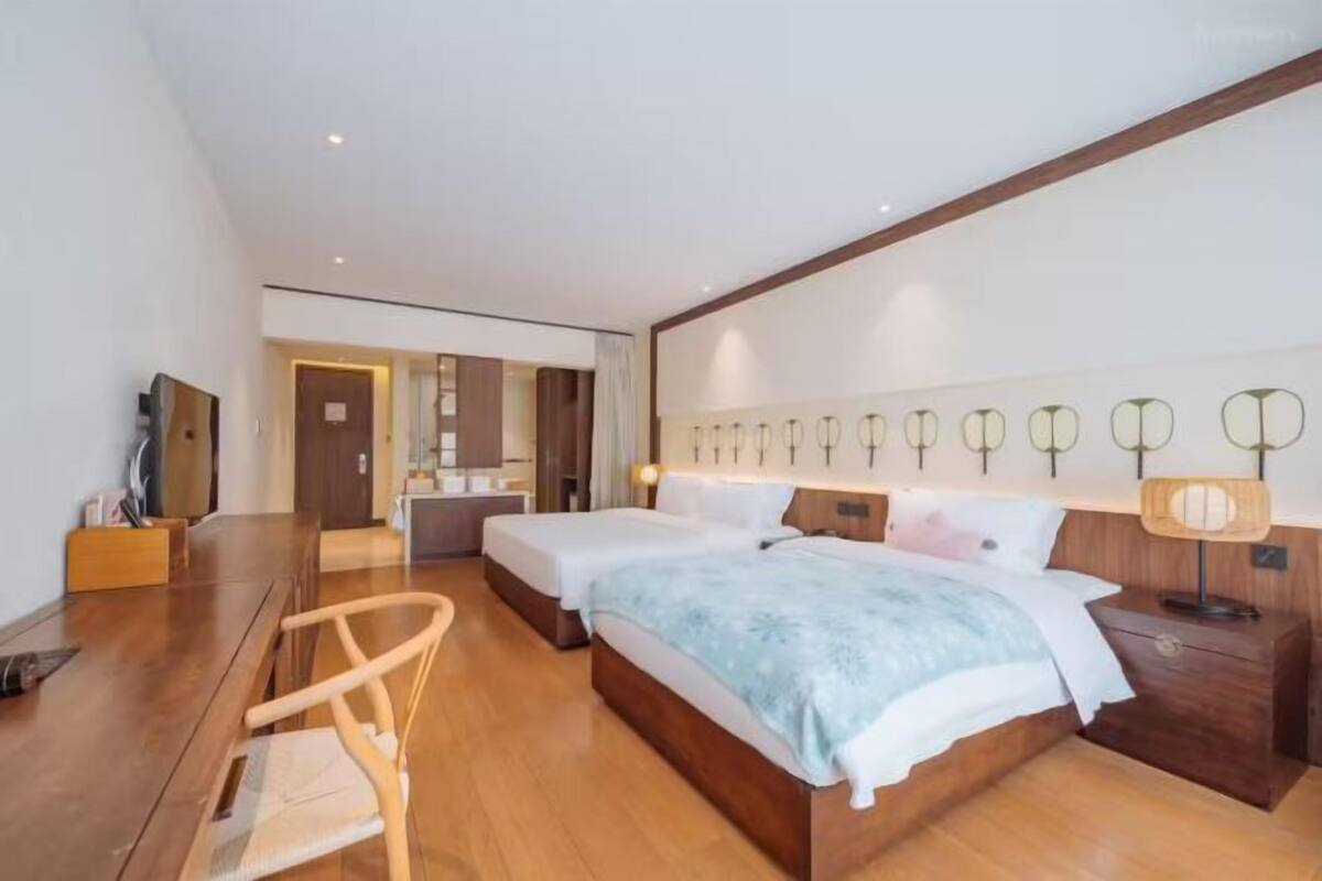 Una habitación de hotel moderna con suelo de madera, dos camas individuales, un escritorio y una silla.
