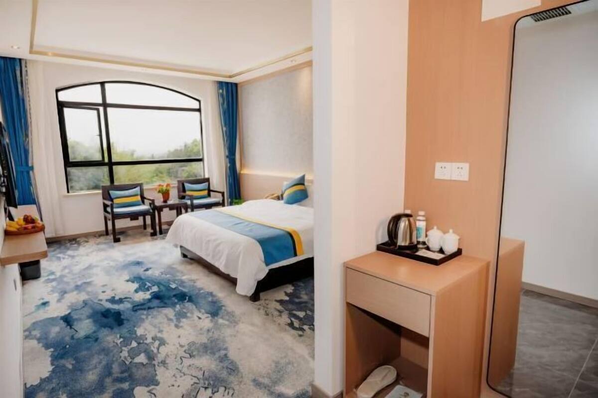 Habitación de hotel con cama, escritorio con espejo, una silla, ventana con cortinas y una mesita con artículos de aseo.