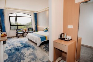 Habitación de hotel con cama, escritorio con espejo, una silla, ventana con cortinas y una mesita con artículos de aseo.