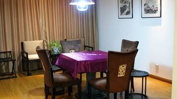 A dining area with a table covered by a purple tablecloth, surrounded by chairs, a hanging light fixture, and framed artwork on the wall.