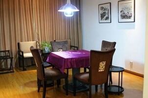 Un comedor con una mesa cubierta por un mantel morado, rodeado de sillas, una lámpara colgante y cuadros en la pared.