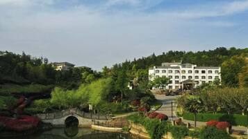 A hotel with a large building, a bridge over a pond, and lush greenery.