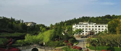 A hotel with a large building, a bridge over a pond, and lush greenery.