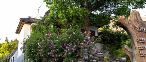 A building with a tree and flowers, a stone wall, and a wooden structure with text.