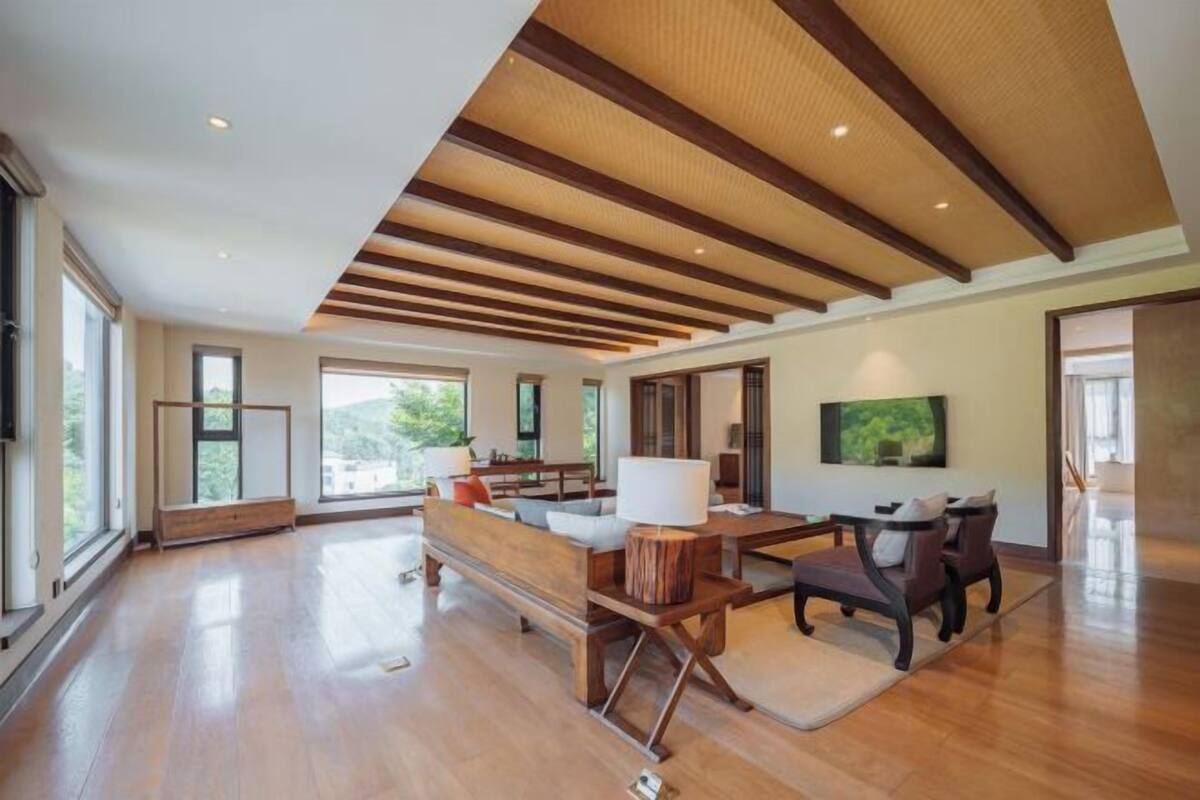 Amplia sala de estar con vigas de madera, ventanas grandes, un sofá, una mesa de centro y un televisor.