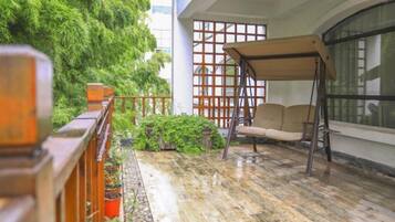 A balcony with a swing chair, potted plants, and a view of a building with a grid-like window design.