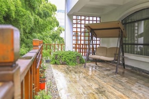 A balcony with a swing chair, potted plants, and a view of a building with a grid-like window design.