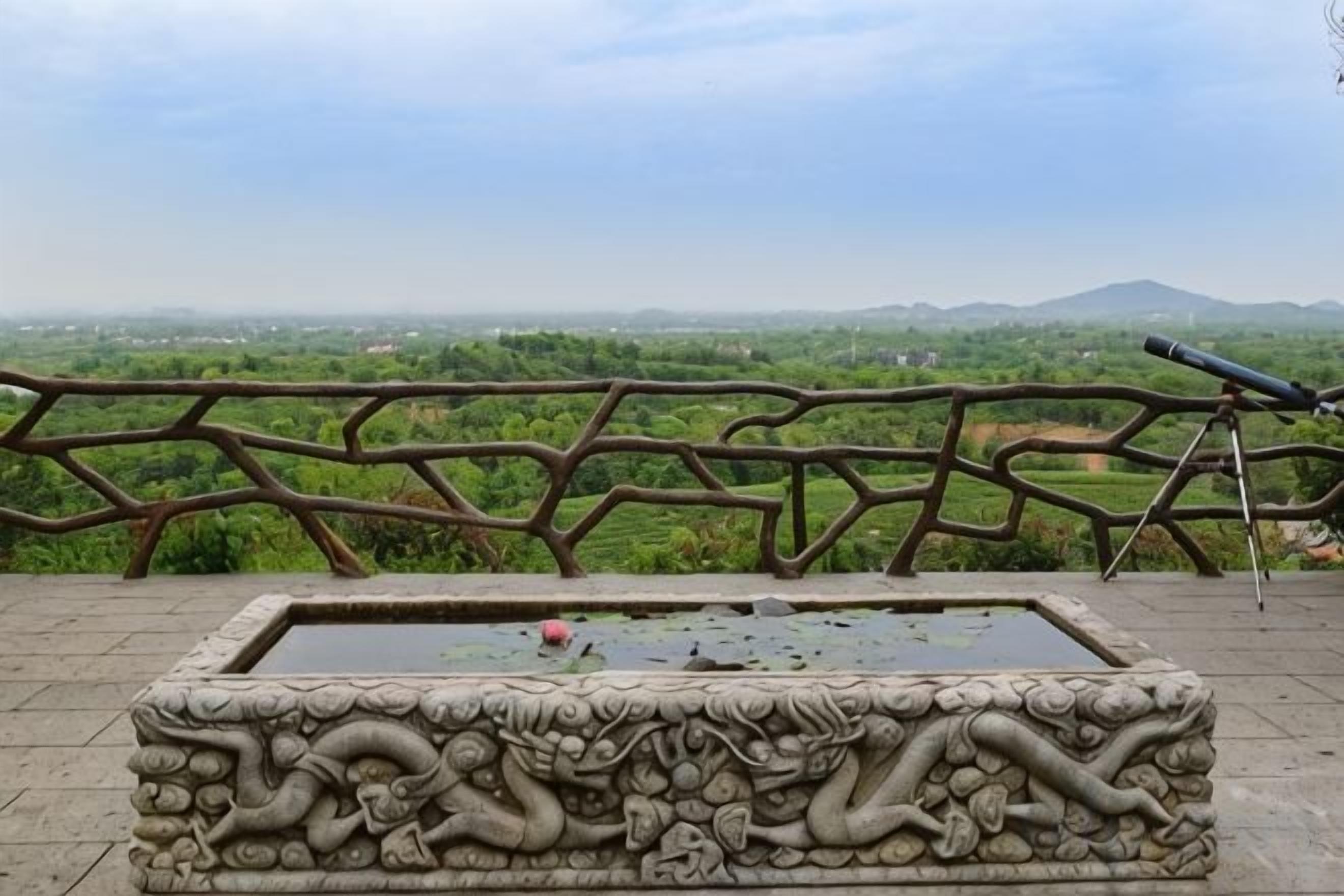 Un banc en pierre orné de sculptures complexes, une rambarde en métal et un télescope.