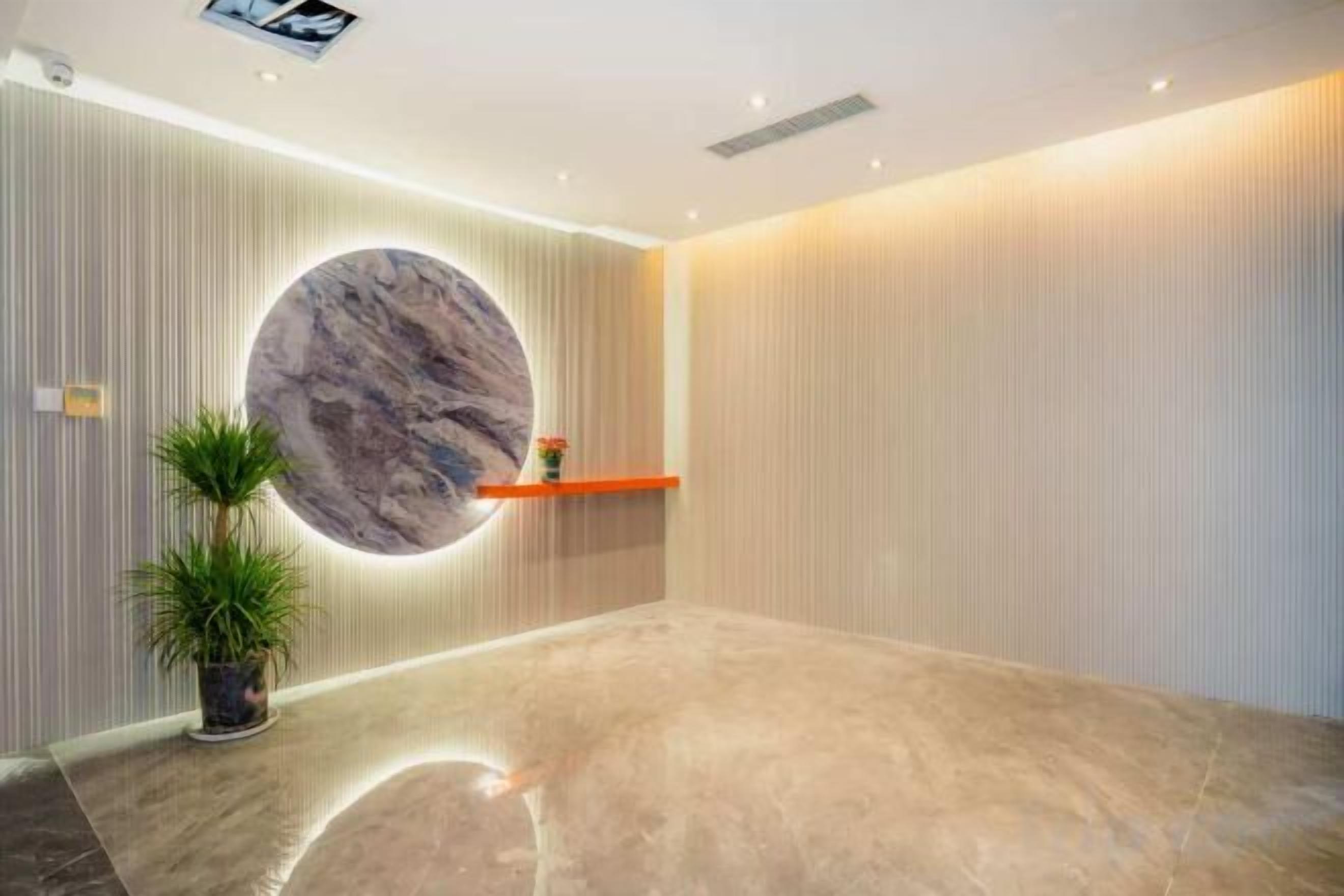 A reception area with a circular marble wall, a potted plant, and a shelf with a vase.