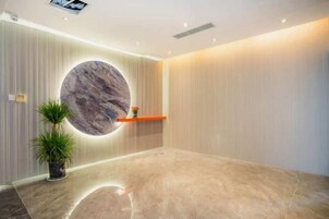 Zona de recepción con un muro circular de mármol, una planta en maceta y una estantería con un jarrón.