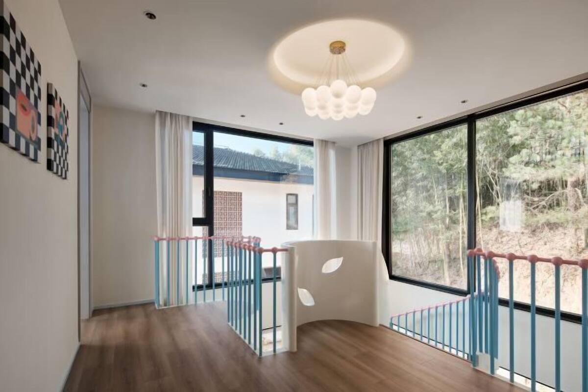 Una habitación moderna con suelo de madera, ventanas amplias, una silla blanca y un aplique de techo.