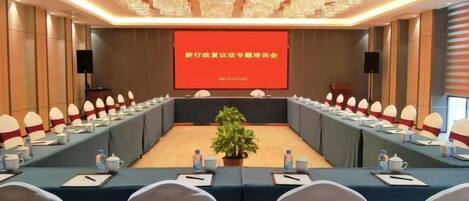 A conference room with a long table, chairs, a projector screen, and a speaker.