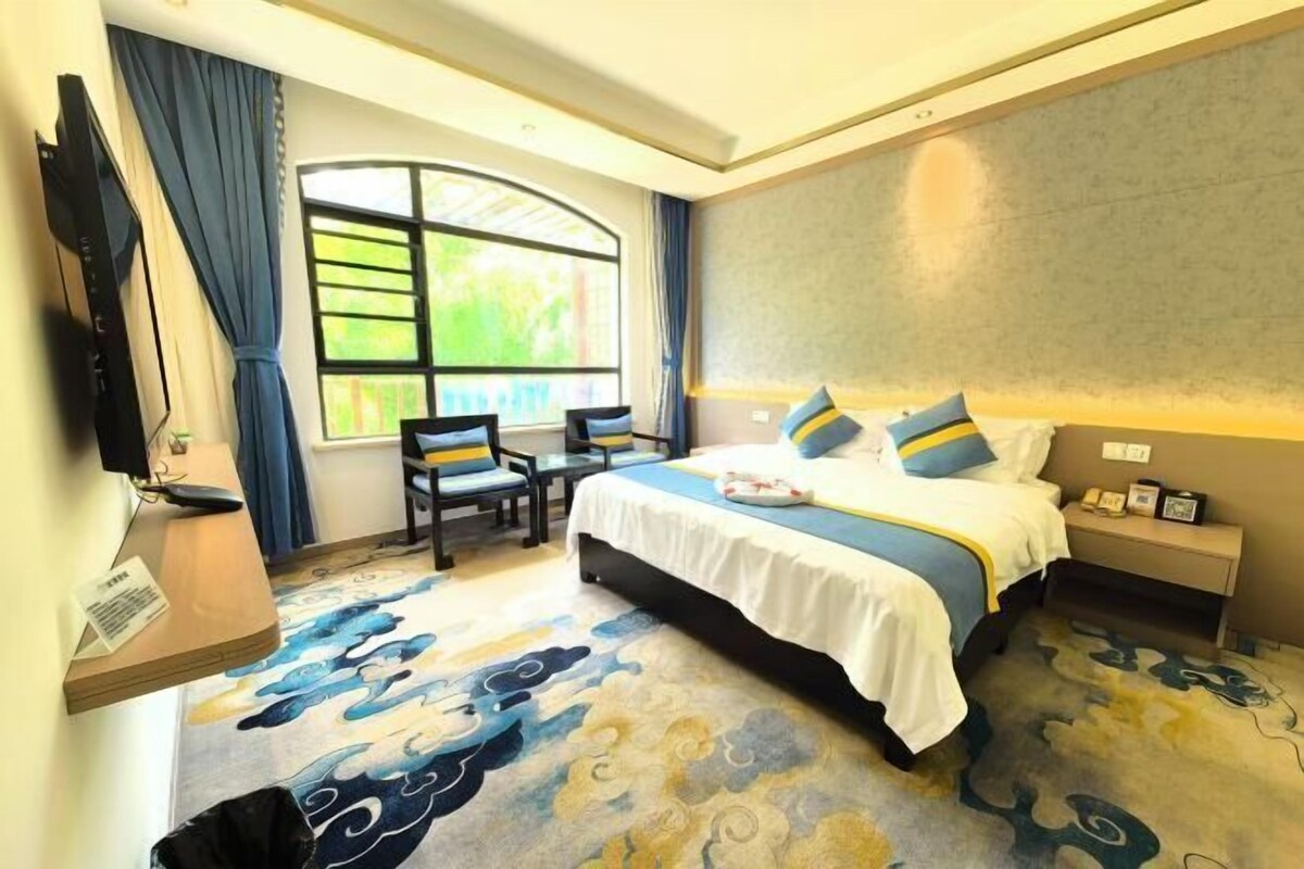 Habitación de hotel con cama, escritorio, silla, televisor y ventana con cortinas.