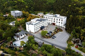 A multi-story building with a parking lot, surrounded by dense greenery. - Ever-Joy Muxin Xiangcun Hotel (Yixing)