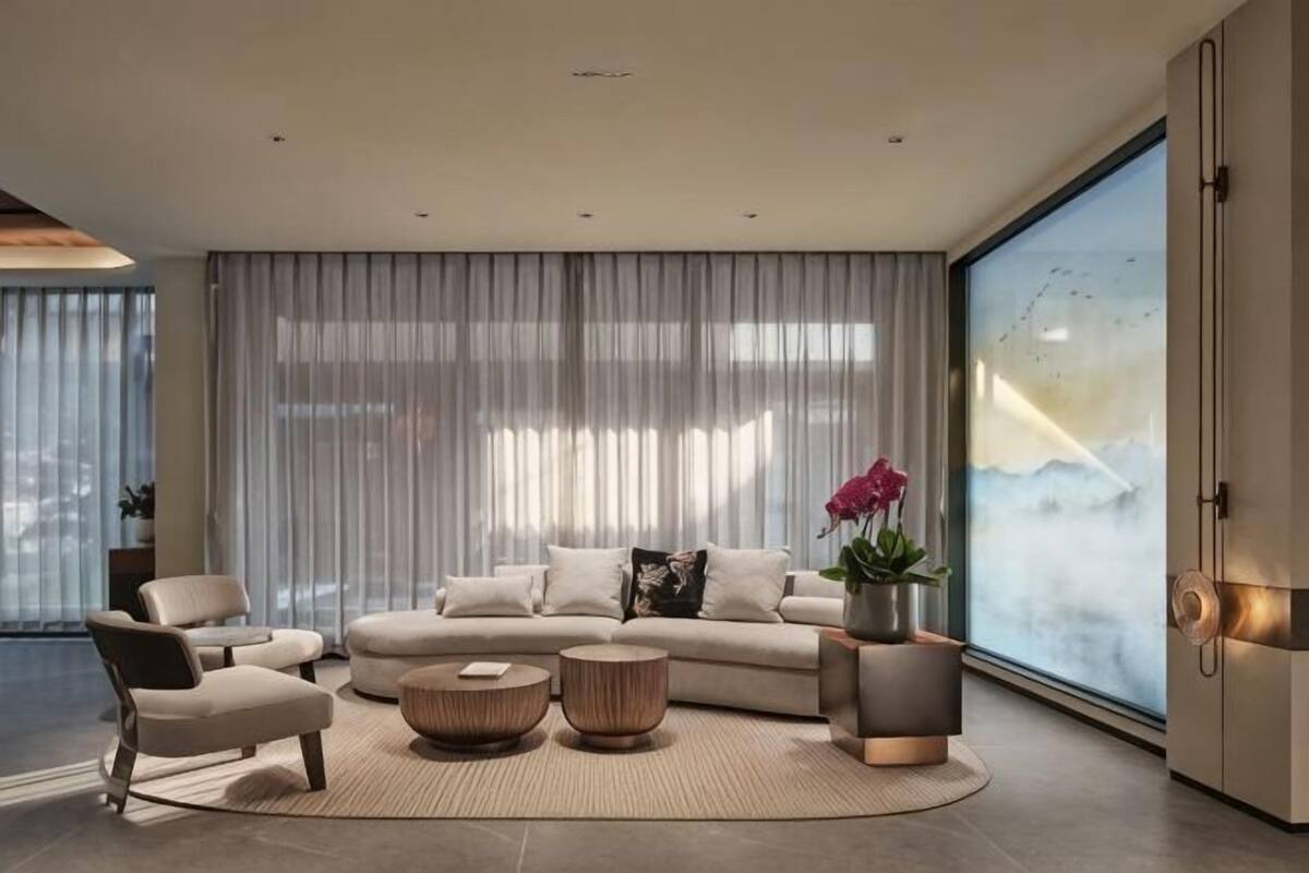 Una sala de estar moderna con un sofá modular, dos sillones, una mesa de centro y un ventanal con cortinas ligeras.