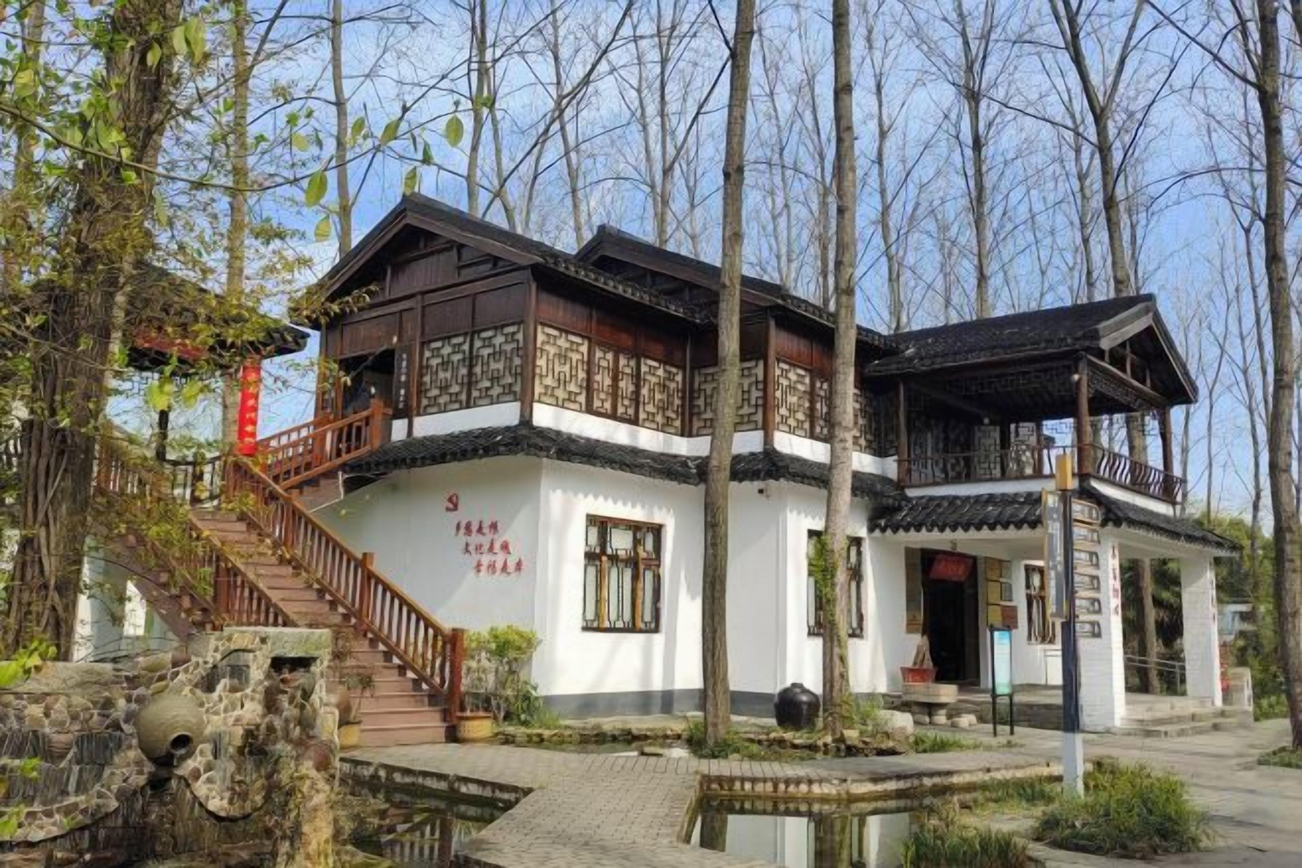 A traditional building with a staircase leading to a balcony, surrounded by trees and a small pond.