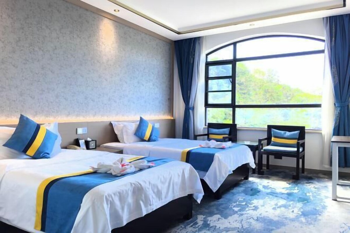 Habitación de hotel con dos camas, un ventanal grande y vistas a zonas verdes.