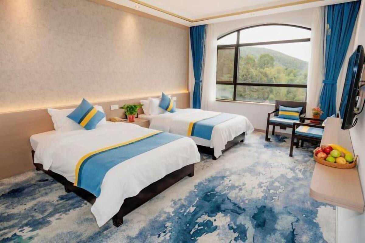 Habitación de hotel con dos camas, un ventanal con vistas, una mesita con fruta y una silla.