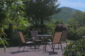 Un patio al aire libre con una mesa y sillas, rodeado de vegetación y vistas a una colina boscosa.