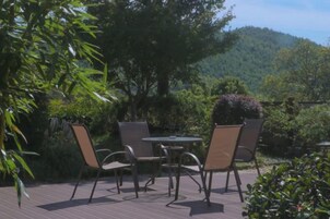 Un patio al aire libre con una mesa y sillas, rodeado de vegetación y vistas a una colina boscosa.