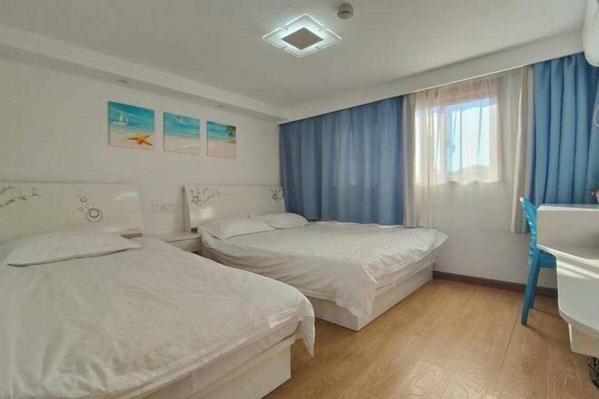 Une chambre d’hôtel avec deux lits simples, un bureau, une chaise et une fenêtre avec des rideaux.