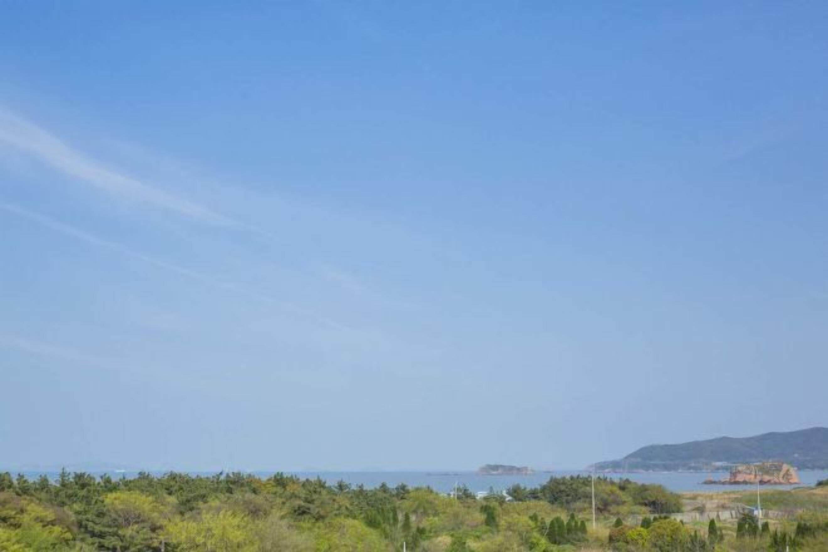 Paisagem costeira com céu limpo, vegetação e edifícios ao longe.