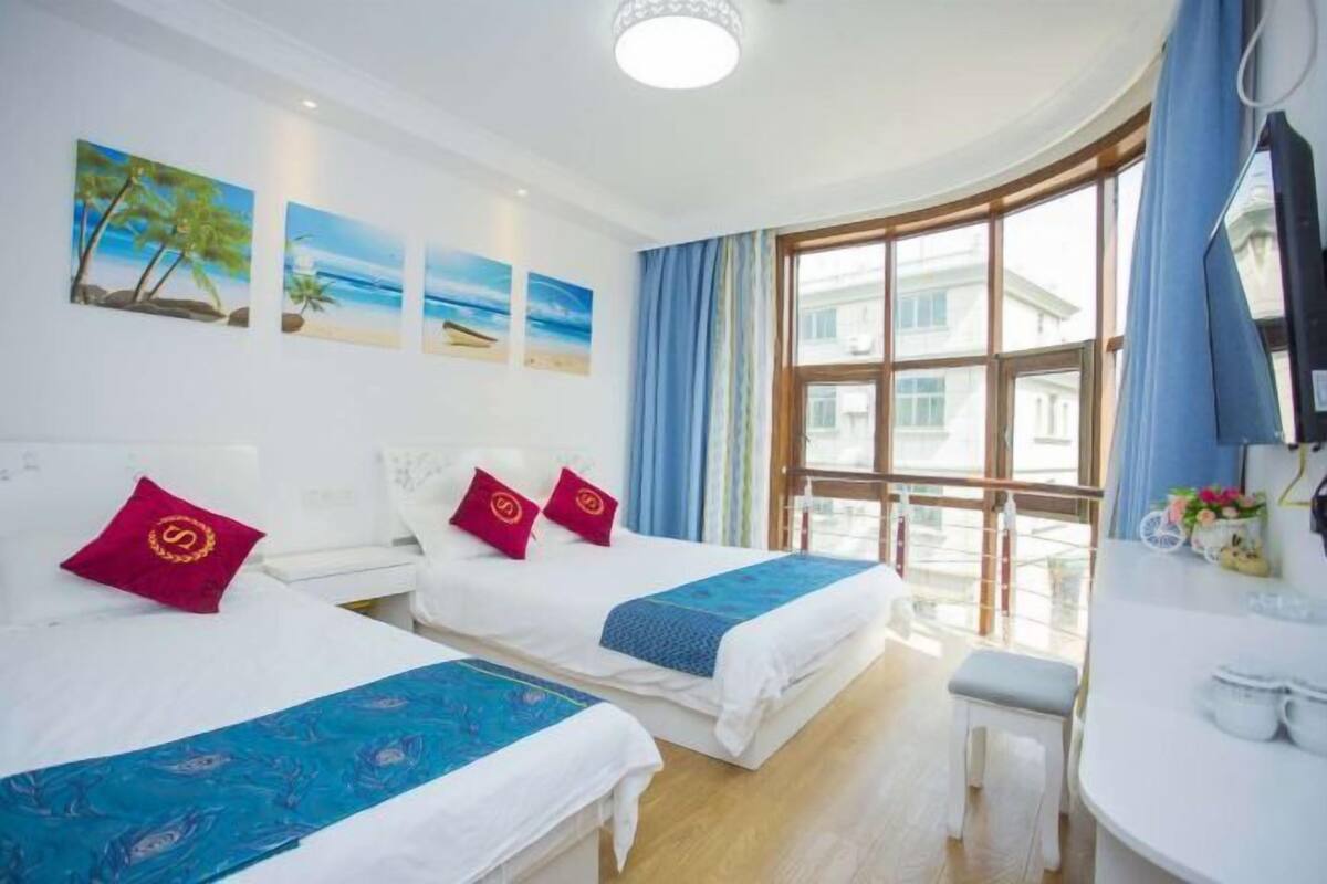 Une chambre d’hôtel avec deux lits, une grande fenêtre donnant sur des immeubles et des œuvres d’art accrochées au mur.