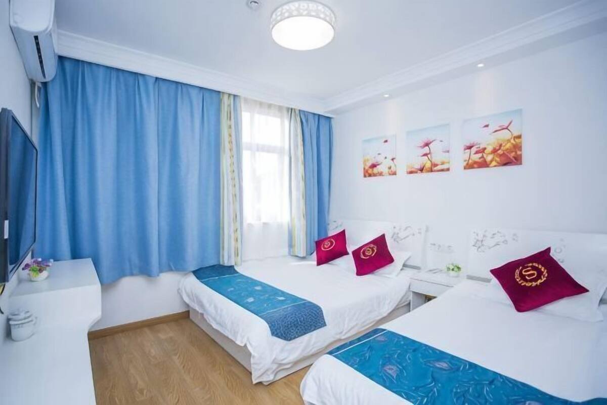 Une chambre d’hôtel avec deux lits, un bureau, une chaise et une fenêtre avec des rideaux.