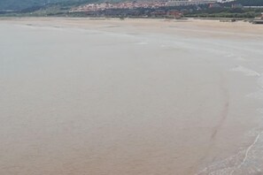 A beach with a wide expanse of sand and a distant view of buildings. - Blue Xinhai Homestay (Shengsi)