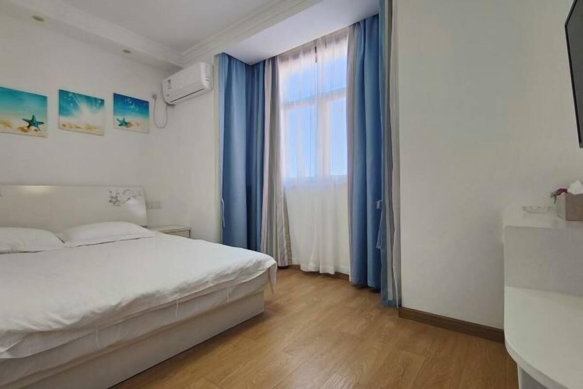 Une chambre à coucher comprenant un lit, une table de chevet, une fenêtre avec des rideaux et un climatiseur fixé au mur.