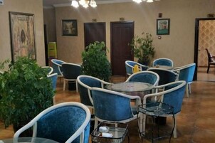 Un hall de hotel con sillas y mesas azules, plantas en macetas y obras de arte enmarcadas en las paredes.