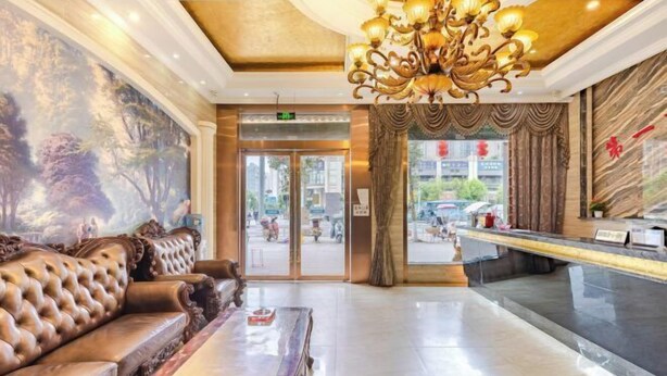 A lobby with a large chandelier, a plush sofa, a reception desk, and a mural on the wall.