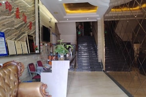 A hotel lobby with a reception desk, a staircase, and a seating area.