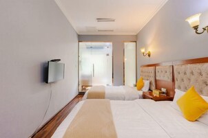 Quarto de hotel com duas camas, televisão e piso de madeira.