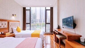 A hotel room with two beds, a desk, a TV, and a large window.