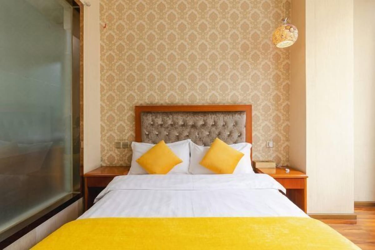 A hotel room with a bed, a nightstand, a lamp, and patterned wallpaper.