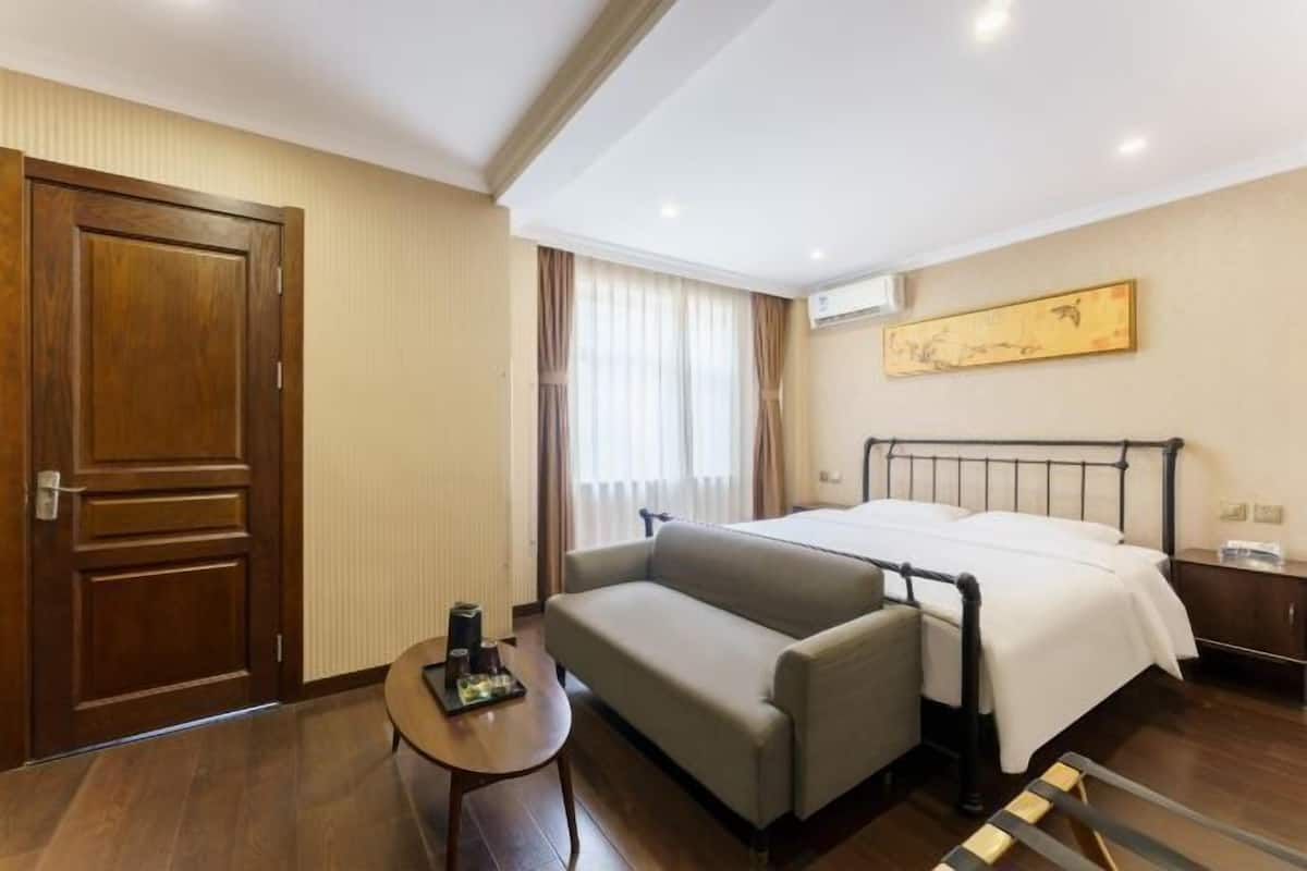 Habitación de hotel con cama, sofá, una mesita, una puerta de madera y ventana con cortinas.