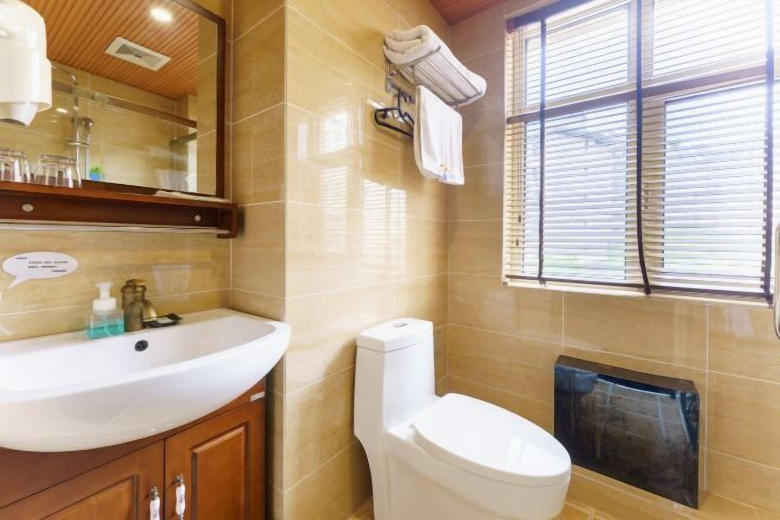 Une salle de bain avec un lavabo blanc, des toilettes, un miroir et une fenêtre avec des stores.