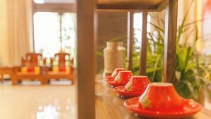 Una hilera de teteras rojas sobre una mesa de madera en una habitación luminosa, con suelo de madera y sillas al fondo.
