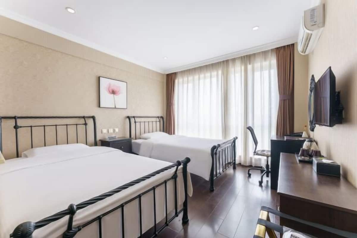 Habitación de hotel con dos camas, un escritorio, una silla, un televisor y una ventana con cortinas.