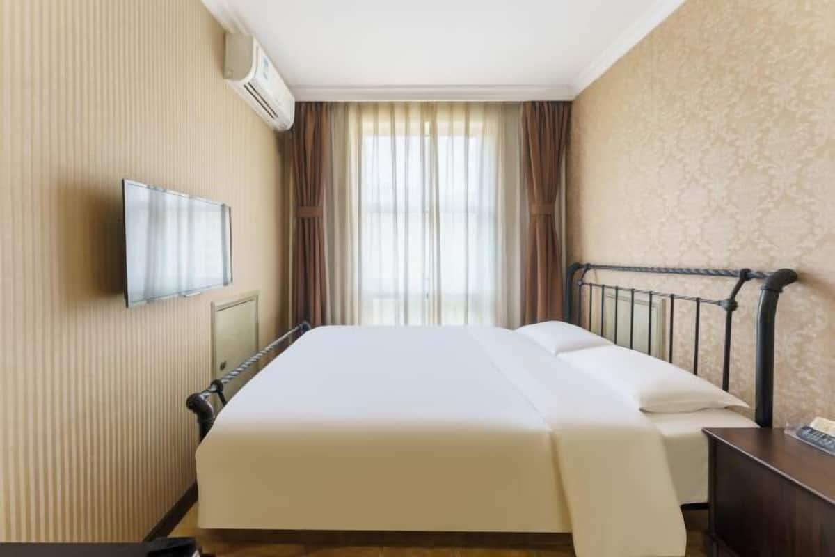Habitación de hotel con cama, televisor de pantalla plana montado en la pared y ventana con cortinas.