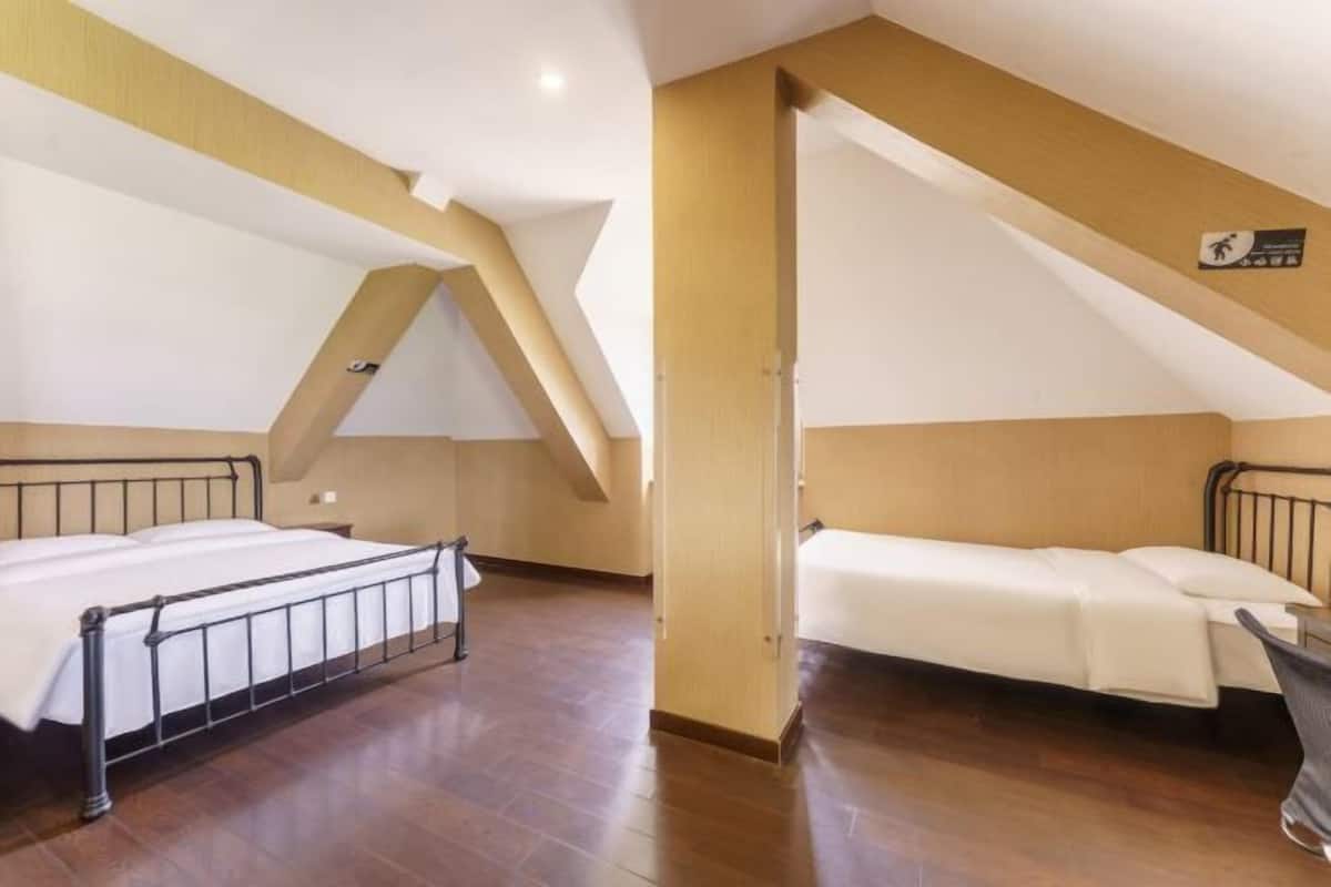 Habitación con dos camas, suelo de madera, techo inclinado y señalización de salida de emergencia visible.