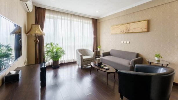 Una habitación de hotel moderna con sofá, sillón, mesa de centro y un gran ventanal con cortinas.