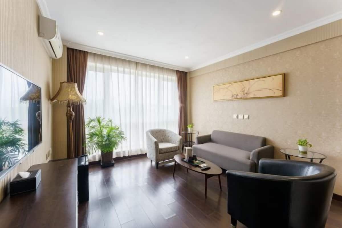 Una habitación de hotel moderna con sofá, sillón, mesa de centro y un gran ventanal con cortinas.