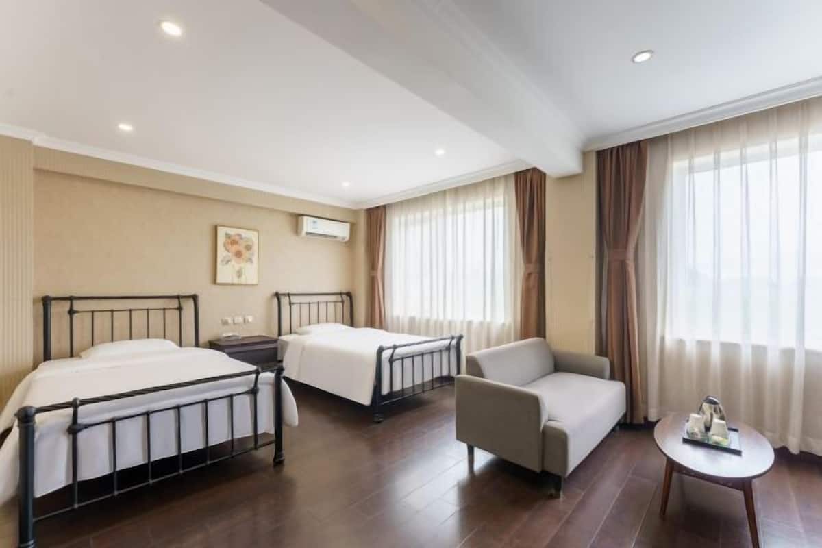 Habitación de hotel con dos camas, un sofá, una mesita y una ventana con cortinas.