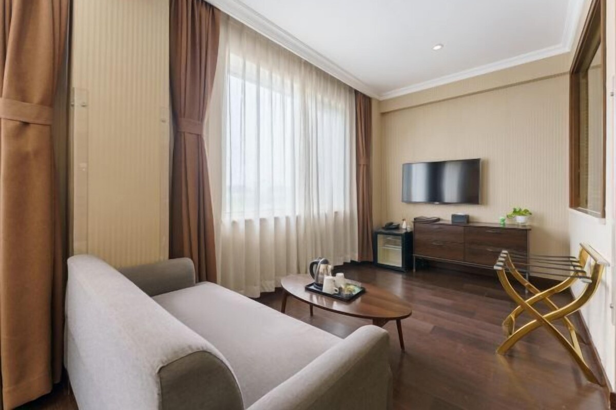 A modern hotel room with a sofa, a coffee table, a TV, and a desk with a chair.