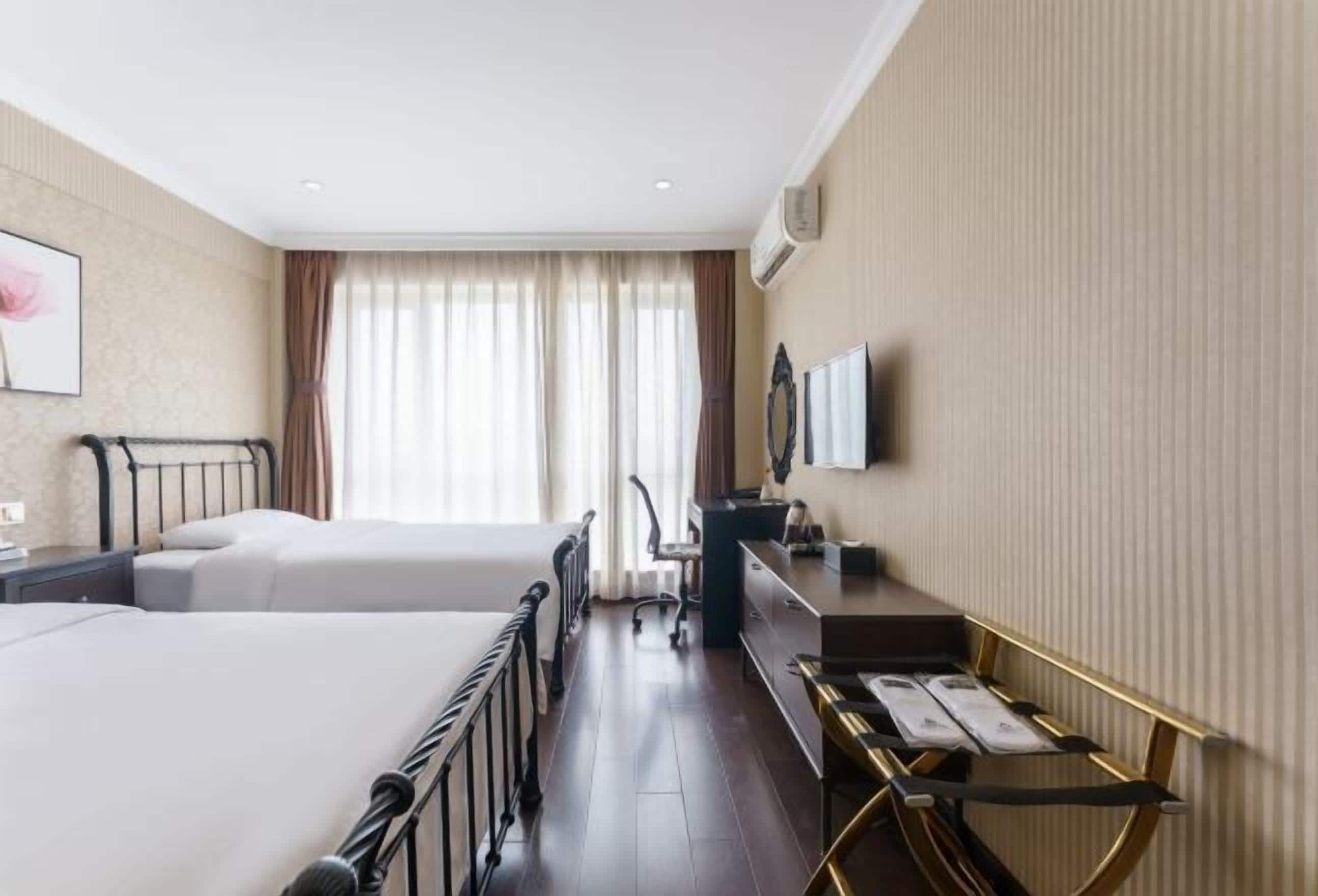 Habitación de hotel con dos camas, un escritorio, una silla, un televisor y una ventana con cortinas.