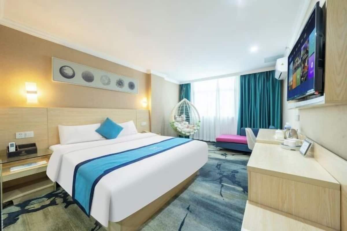 Ein Hotelzimmer mit Bett, Nachttisch, Fernseher und Schreibtisch mit Stuhl.