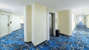 Een hotelgang met een blauw gestreept tapijt, crèmekleurige muren en deuren die naar kamers leiden.