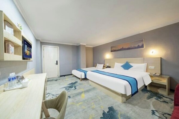 A hotel room with two beds, a desk, a chair, a bookshelf, and a painting on the wall.